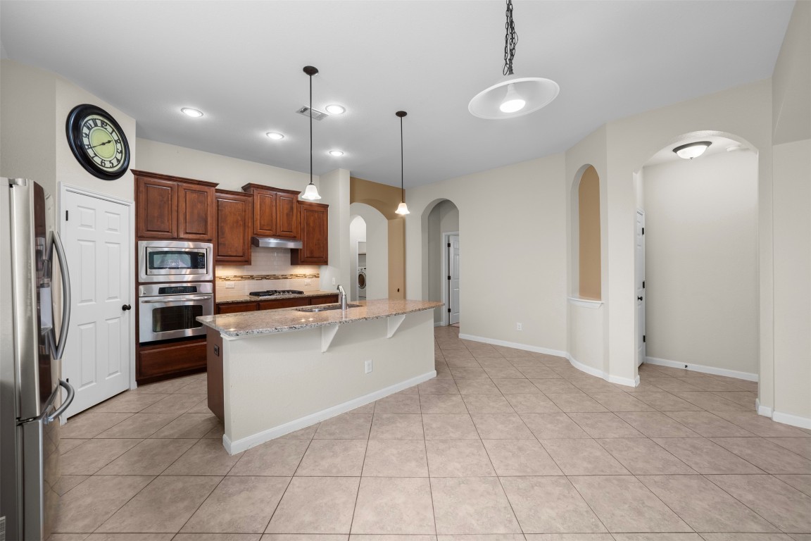 216 Archipelago Trail Austin, TX 78717 - Photo 11 of 40 Kitchen with backsplash, stainless steel appliances, a breakfast bar, hanging light fixtures, and light stone counters