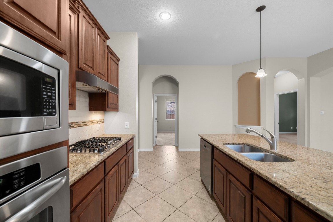 216 Archipelago Trail Austin, TX 78717 - Photo 15 of 40 Kitchen featuring stainless steel appliances, light stone counters, decorative light fixtures, light tile patterned flooring, and tasteful backsplash
