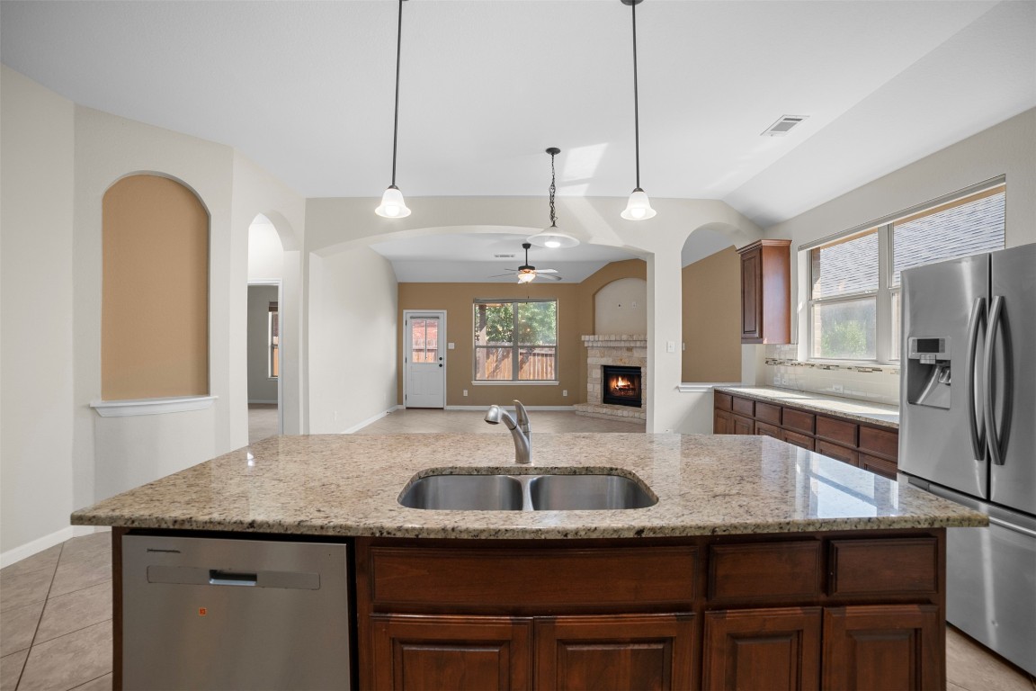 216 Archipelago Trail Austin, TX 78717 - Photo 16 of 40 Kitchen featuring a center island with sink, stainless steel appliances, pendant lighting, a ceiling fan, and a brick fireplace