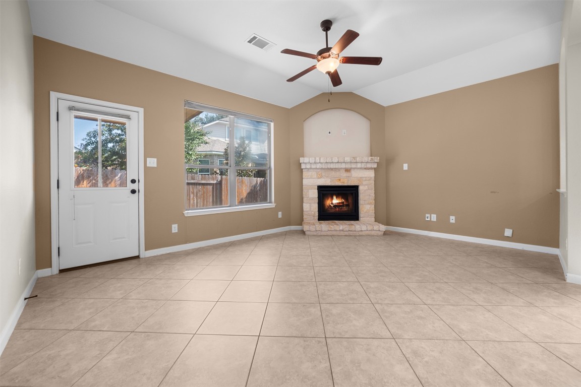 216 Archipelago Trail Austin, TX 78717 - Photo 17 of 40 Unfurnished living room featuring a stone fireplace, a ceiling fan, light tile patterned floors, and lofted ceiling