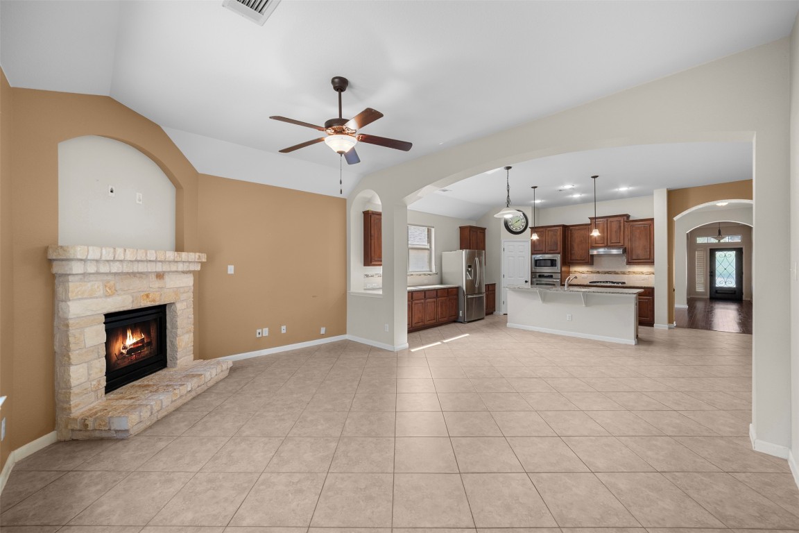 216 Archipelago Trail Austin, TX 78717 - Photo 18 of 40 Unfurnished living room featuring a ceiling fan, arched walkways, a fireplace, light tile patterned floors, and vaulted ceiling