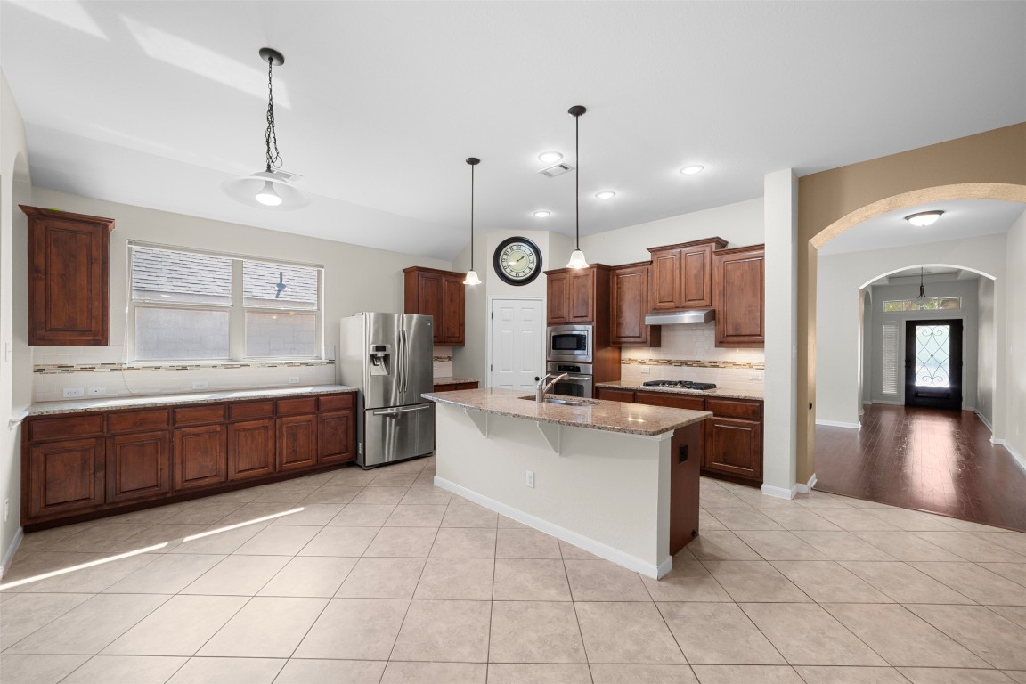 216 Archipelago Trail Austin, TX 78717 - Photo 10 of 40 Kitchen with tasteful backsplash, arched walkways, hanging light fixtures, light stone counters, and recessed lighting