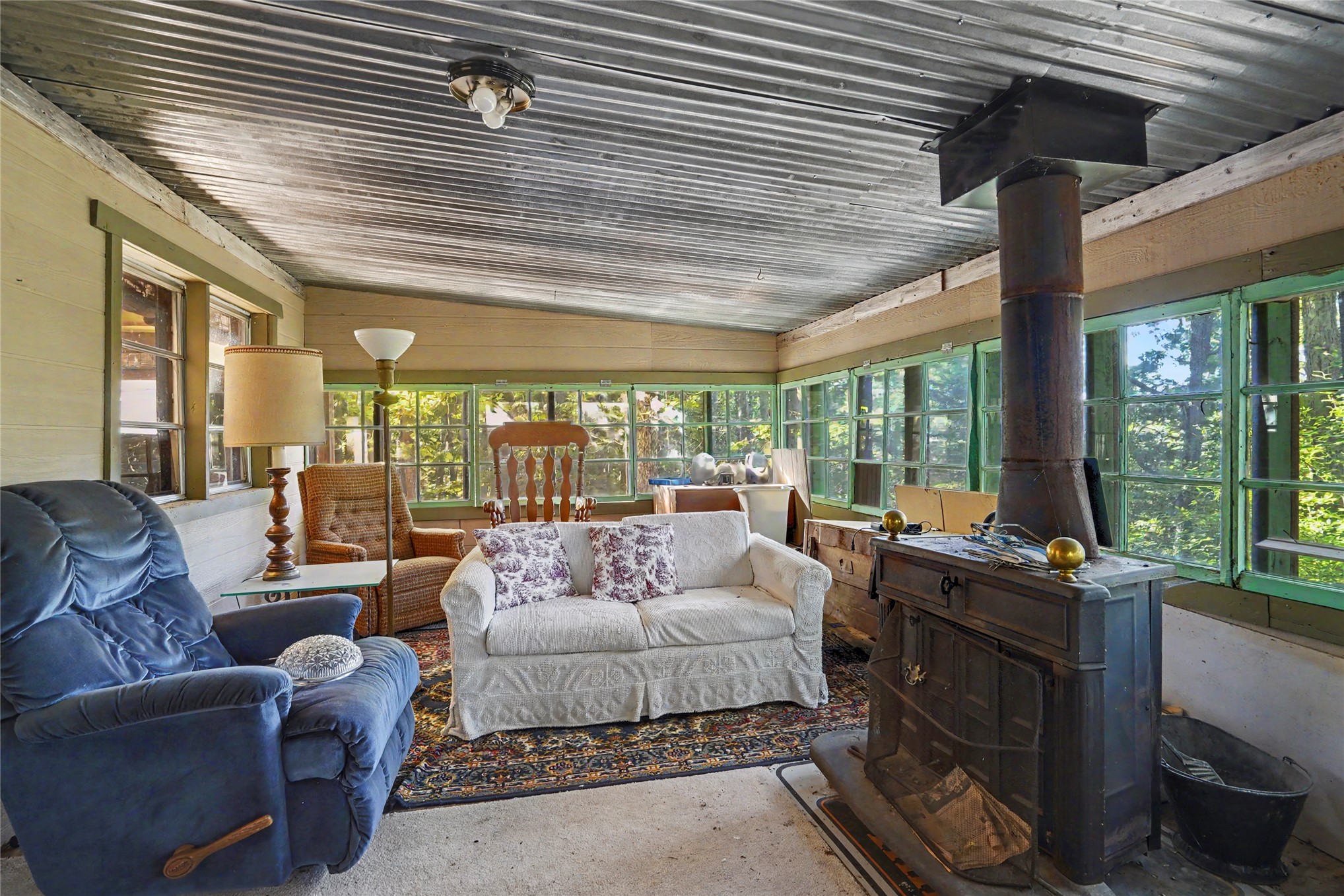 46420 South 590 Road Jay, OK 74346 - Photo 46 of 63 Room featuring exposed corrugated metal ceiling, extensive window coverage, and a built-in wood-burning stove with a chimney