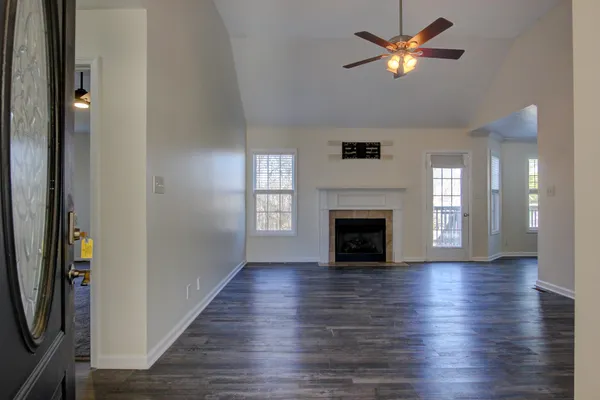 an empty room with wooden floor a ceiling fan a fireplace and windows
