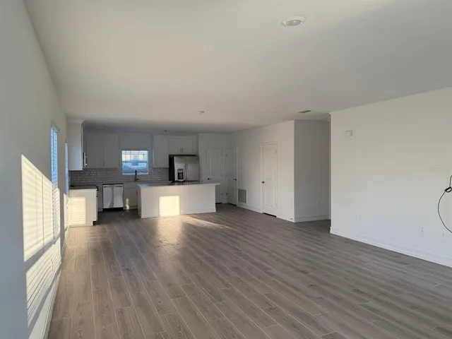 a view of empty room with wooden floor and kitchen view