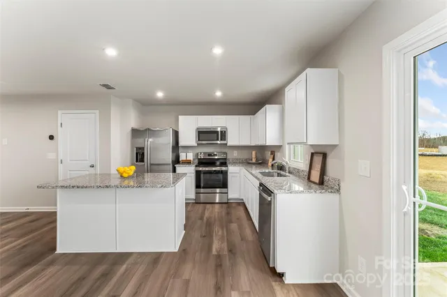 a kitchen with stainless steel appliances a refrigerator a sink dishwasher a oven with white cabinets and wooden floor