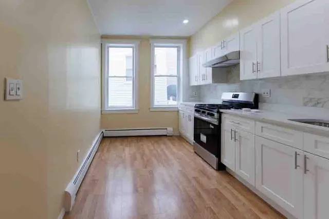 a kitchen with granite countertop a stove a sink and white cabinets with wooden floor