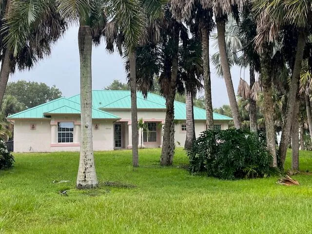 a view of a white house with a big yard and palm trees