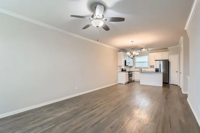 an empty room with wooden floor chandelier fan and windows