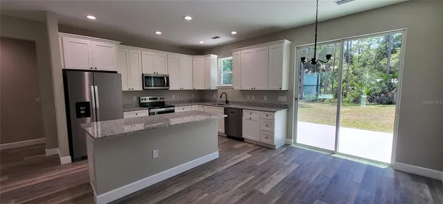 a kitchen with stainless steel appliances granite countertop a refrigerator a sink dishwasher a stove and white countertops with wooden floor