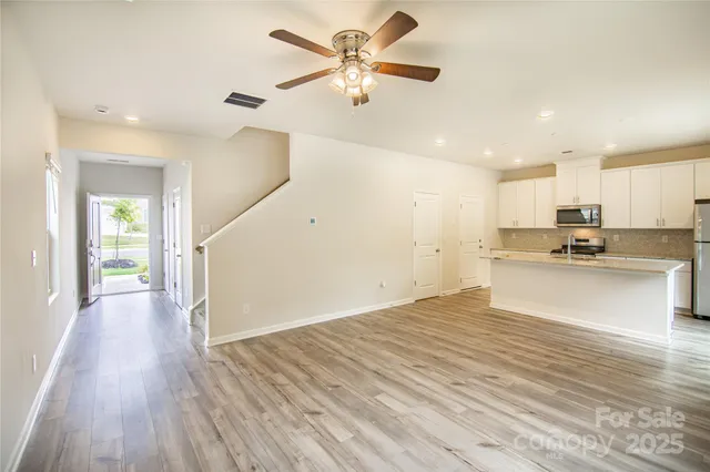 a view of an empty room and kitchen with wooden floor