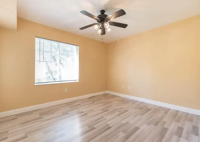 an empty room with wooden floor fan and windows