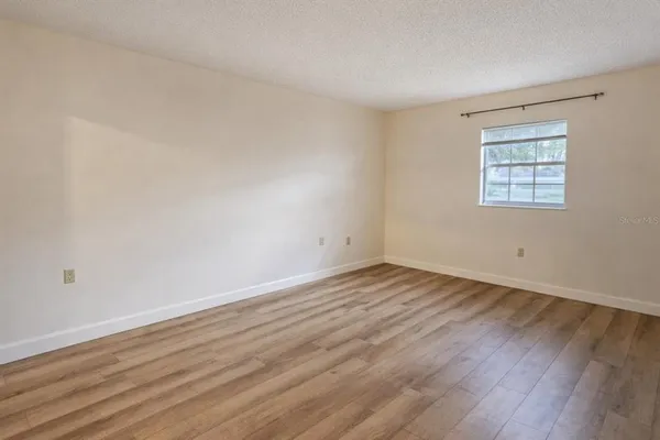 a view of an empty room with wooden floor and a window