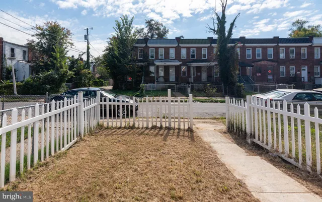 a view of a brick house with large trees and wooden fence