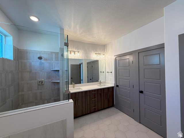 8087 South 615 East, Unit 3 Sandy, UT 84070 - Photo 13 of 23 Spacious bathroom featuring a glass-enclosed shower with tile surround and built-in shelving, a dual vanity with a quartz countertop, wood-finish cabinetry, and hexagon tile flooring