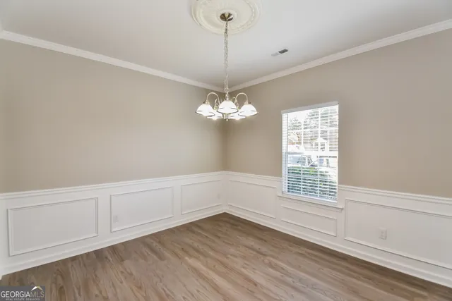a view of an empty room with chandelier fan and wooden floor