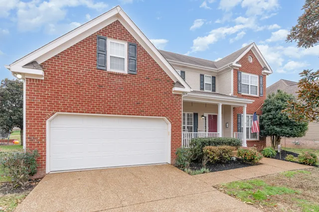a view of a brick house with a yard plants and large tree