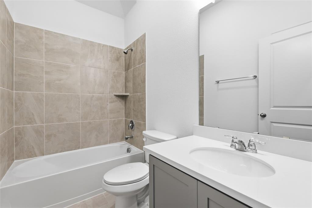 2529 Rivers W Road Anna, TX 75409 - Photo 5 of 40 Bathroom featuring a white bathtub, ceramic tile surround with built-in shelf, gray vanity with white countertop, and chrome fixtures