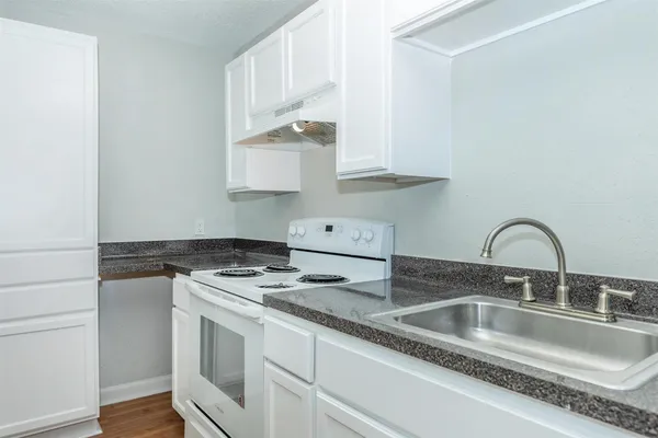 a kitchen with stainless steel appliances granite countertop a sink stove and white cabinets with wooden floor