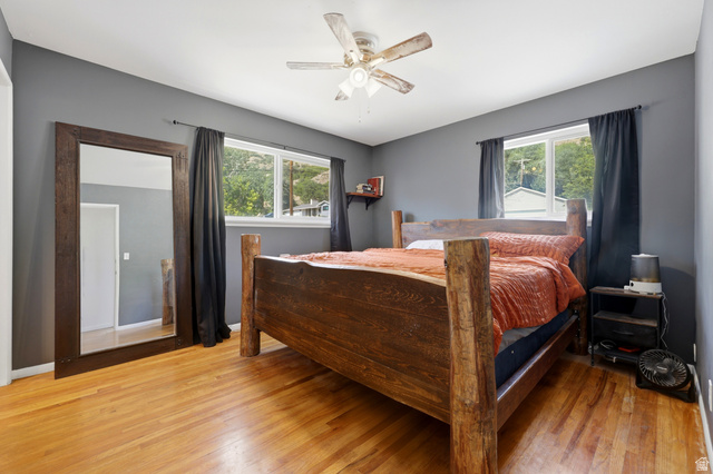 1486 3rd Street Ogden, UT 84404 - Photo 11 of 26 Room featuring wood-finish flooring, two large windows with dark drapery, a ceiling fan, and painted gray walls
