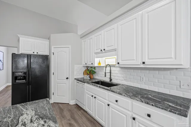 a kitchen with granite countertop a sink stainless steel appliances white cabinets and a window