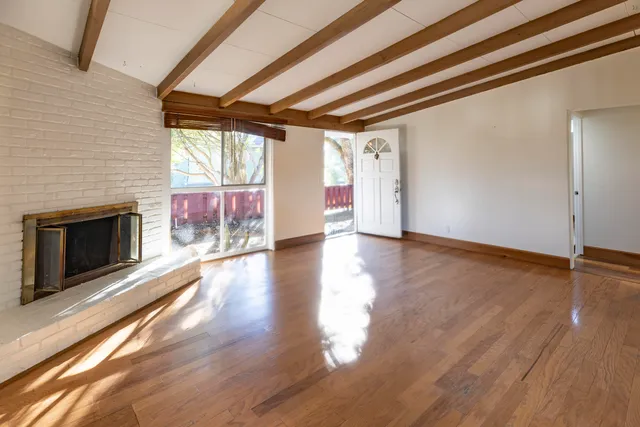 an empty room with wooden floor fireplace and windows