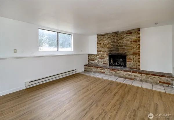 an empty room with wooden floor fireplace and windows