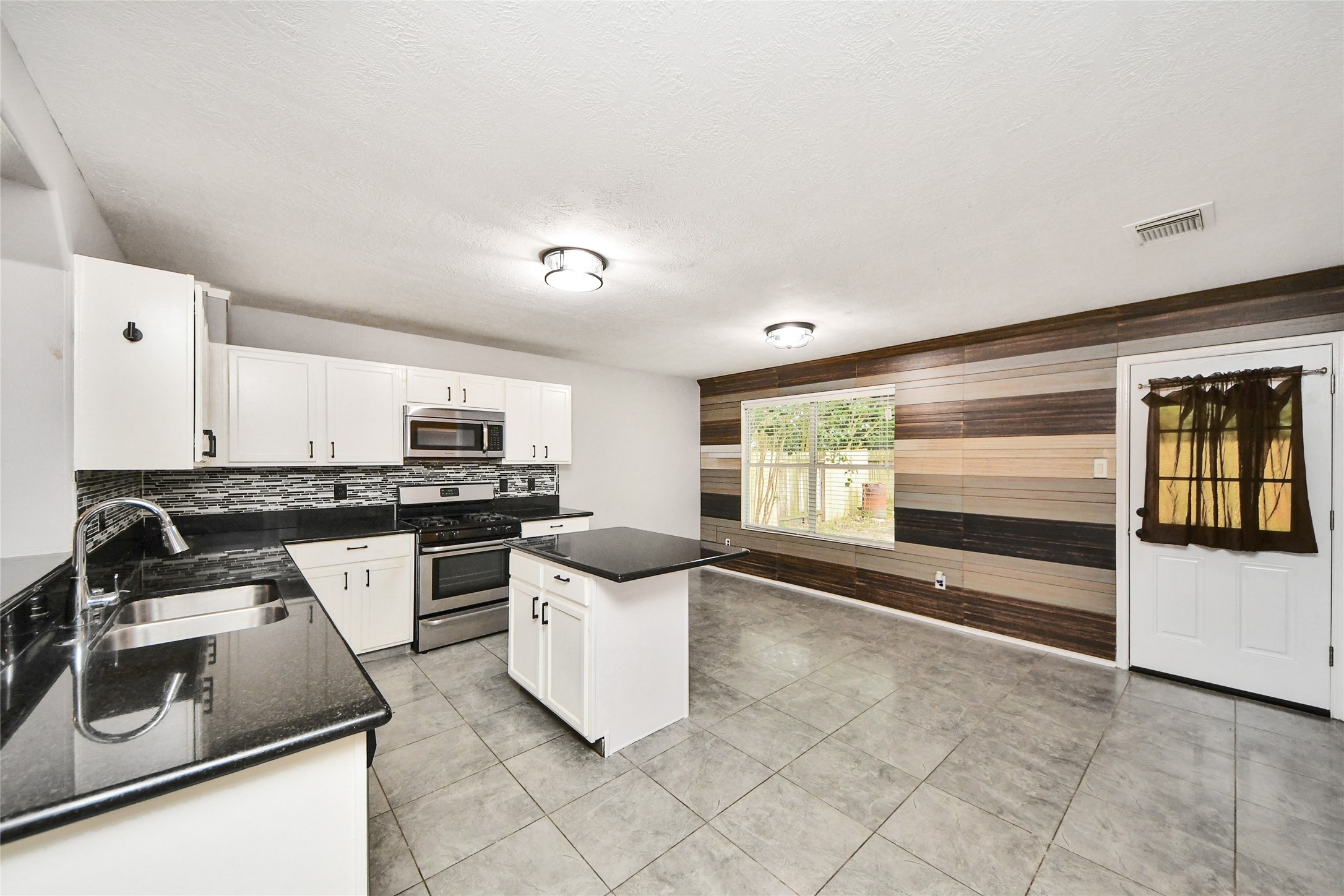 24019 Kingbriar Drive Spring, TX 77373 - Photo 14 of 41 This modern kitchen boasts crisp white cabinetry, sleek black granite-style countertops, and a stylish subway tile backsplash, all centered around a functional island.