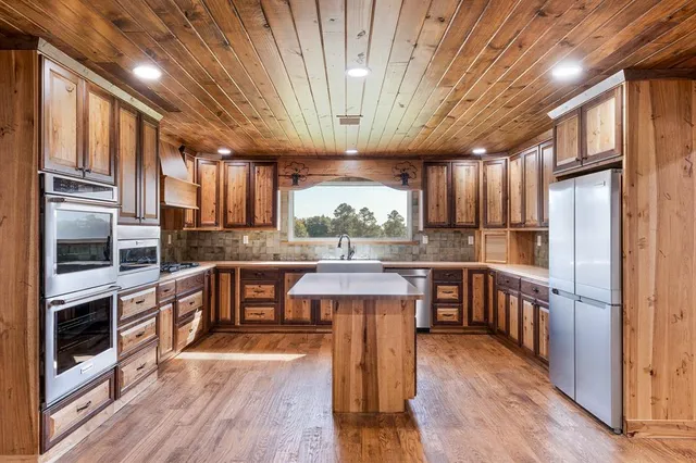 a kitchen with stainless steel appliances granite countertop a refrigerator a sink dishwasher a stove and white countertops with wooden floor