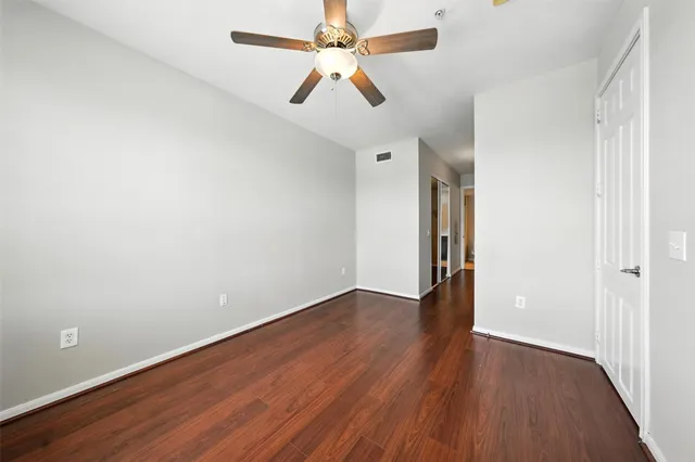 an empty room with wooden floor and a ceiling fan