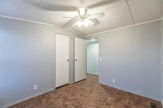an empty room with a ceiling fan and kitchen view