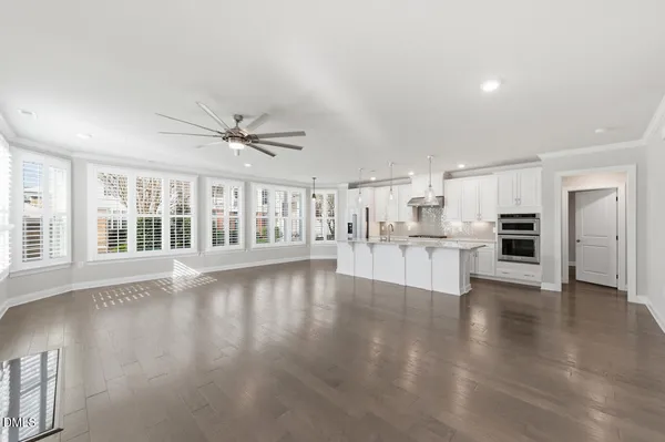 a view of an empty room with wooden floor and a kitchen