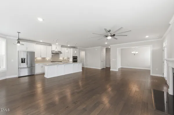 a view of an empty room with wooden floor and a kitchen