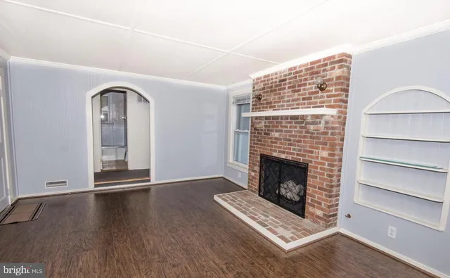 a view of an empty room with wooden floor fireplace and a window