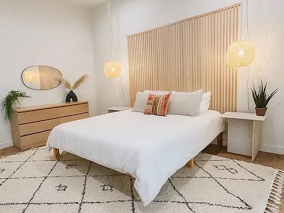 a bedroom with a bed a table and a large mirror next to a window