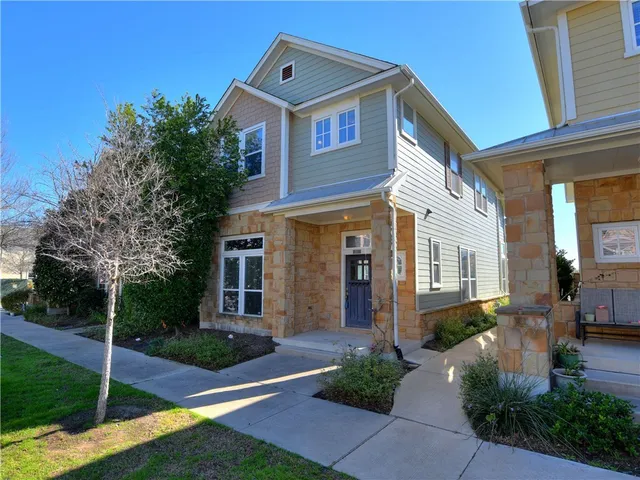 a view of a brick house with a yard plants and large tree
