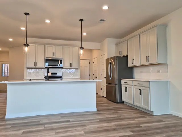 a kitchen with stainless steel appliances kitchen island granite countertop a refrigerator a stove a sink and white cabinets with wooden floor