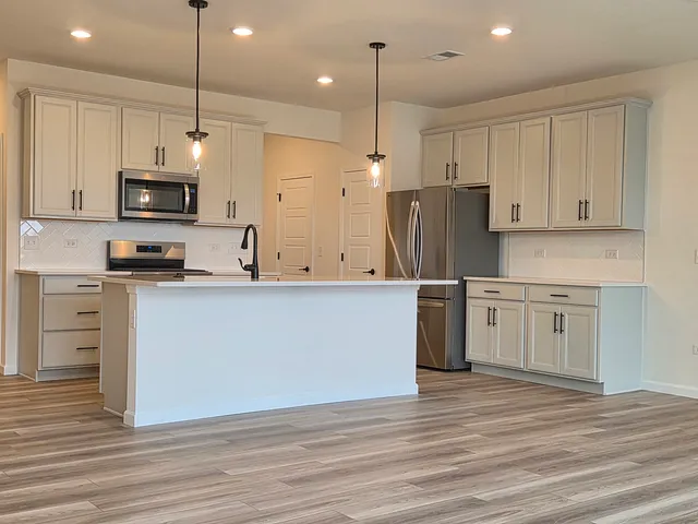 a kitchen with stainless steel appliances granite countertop a stove a sink a refrigerator and white cabinets with wooden floor