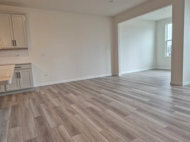 a view of empty room with wooden floor and kitchen