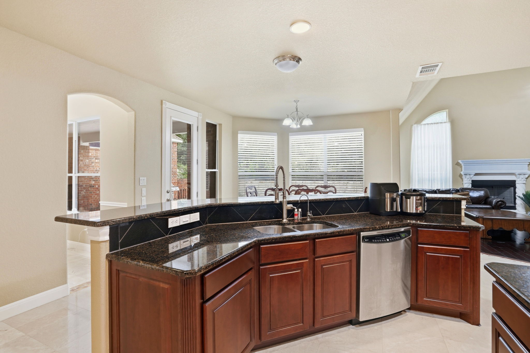 222 Vailco Lane Austin, TX 78738 - Photo 18 of 39 Kitchen featuring granite countertops, wood cabinetry, a double basin sink with a gooseneck faucet, a stainless steel dishwasher, and a tile backsplash