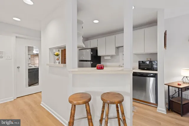 a kitchen with stainless steel appliances kitchen island granite countertop a refrigerator a stove and white cabinets with wooden floor