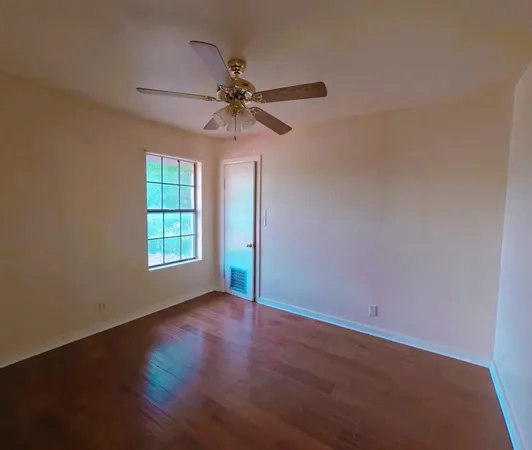 an empty room with wooden floor fan and windows