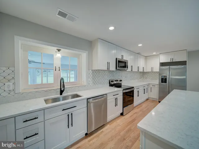 a kitchen with stainless steel appliances a sink dishwasher a stove top oven a refrigerator with wooden cabinets and floor