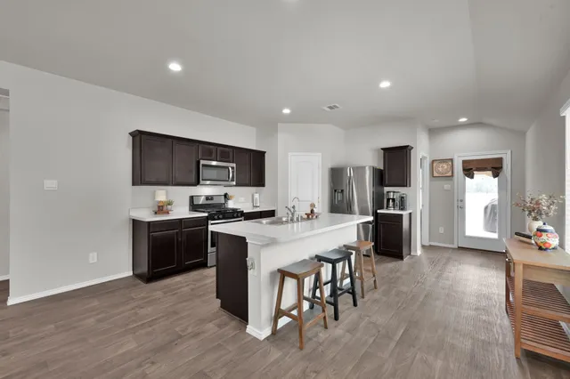 a kitchen with stainless steel appliances kitchen island granite countertop a stove top oven a sink a dining table and chairs with wooden floor