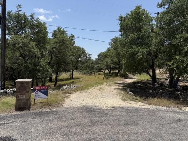 242 Landons Way Georgetown, TX 78633 - Photo 1 of 30 Mature trees line a gravel path, inviting exploration of this generous lot.