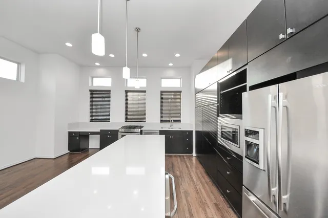 a large kitchen with a large window a refrigerator and wooden floor