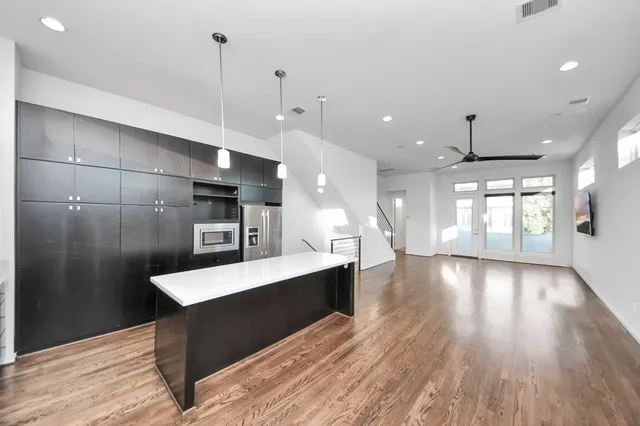 a large kitchen with stainless steel appliances a large counter top a refrigerator and a wooden floor