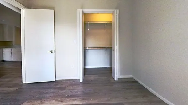 a view of an empty room with wooden floor and a bedroom