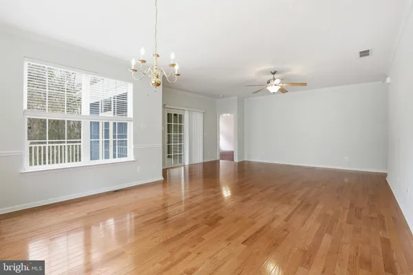 a view of an empty room with chandelier fan and wooden floor