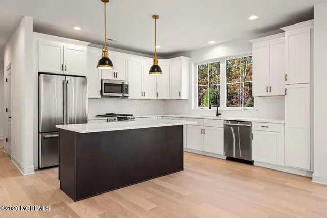 a kitchen with stainless steel appliances granite countertop a refrigerator a sink dishwasher a stove and white countertops with wooden floor